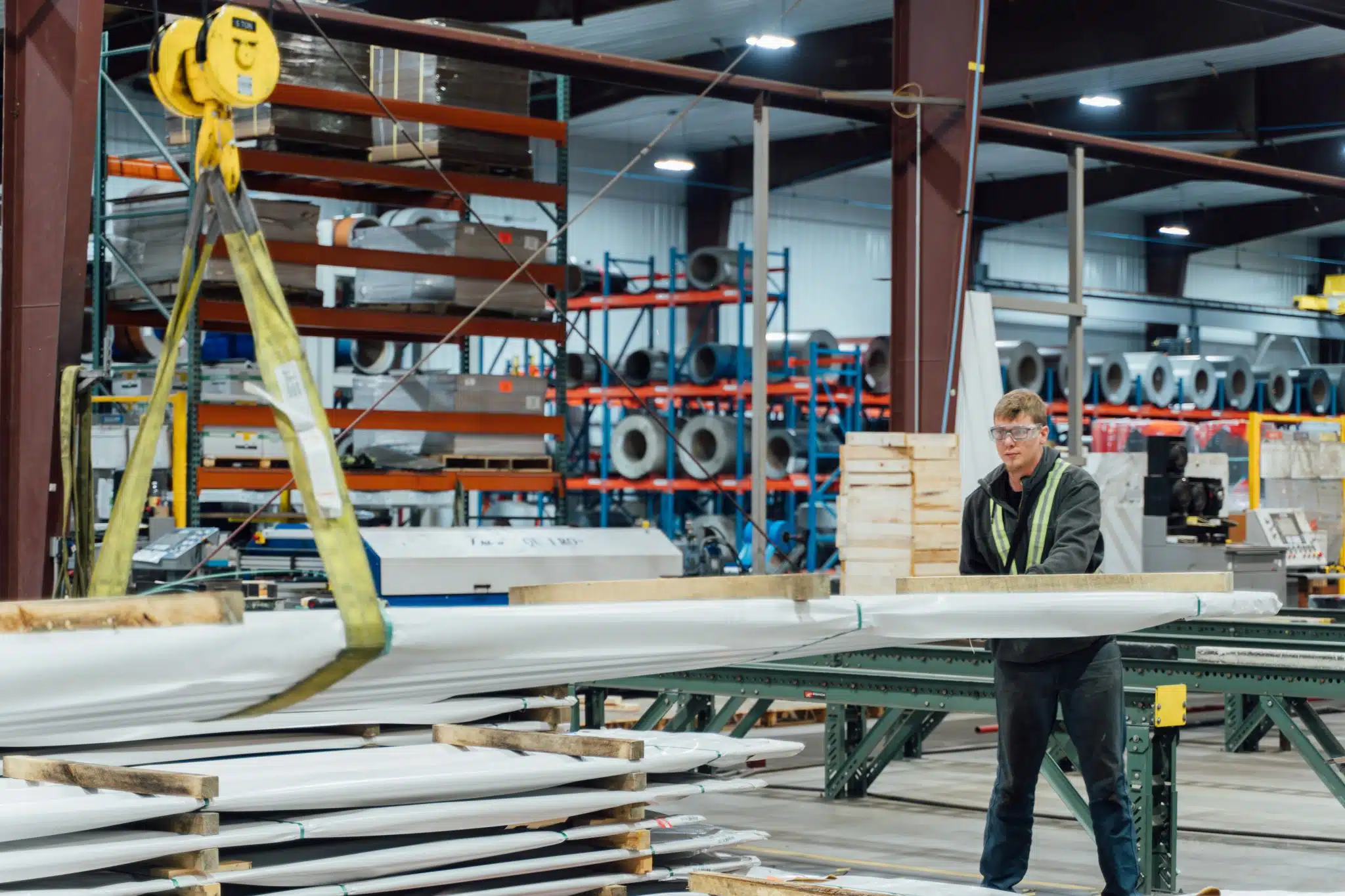 Employee at manufacturing plant using a crane to move metal panels